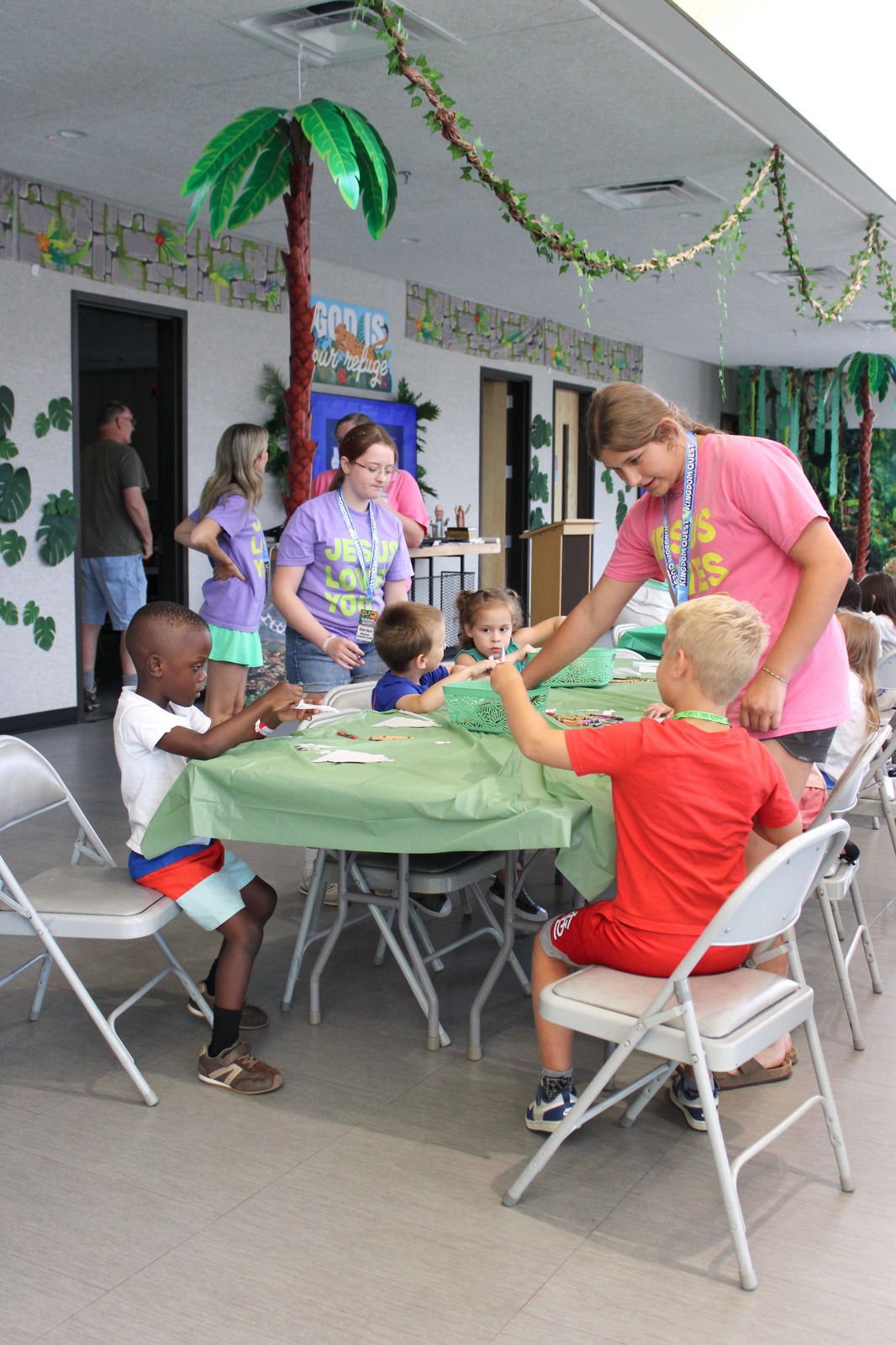 Older attendee helping younger children with a craft at VBS
